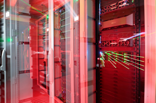 In rotes Licht getaucht ist ein Serverschrank zu erkennen, in dessen Glasabdeckung sich grüne Lichteffekte spiegeln. 